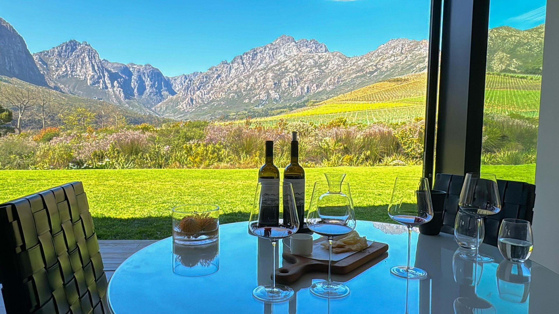 Wine bottles and glasses on a table, with a mountain vineyard view through the window.