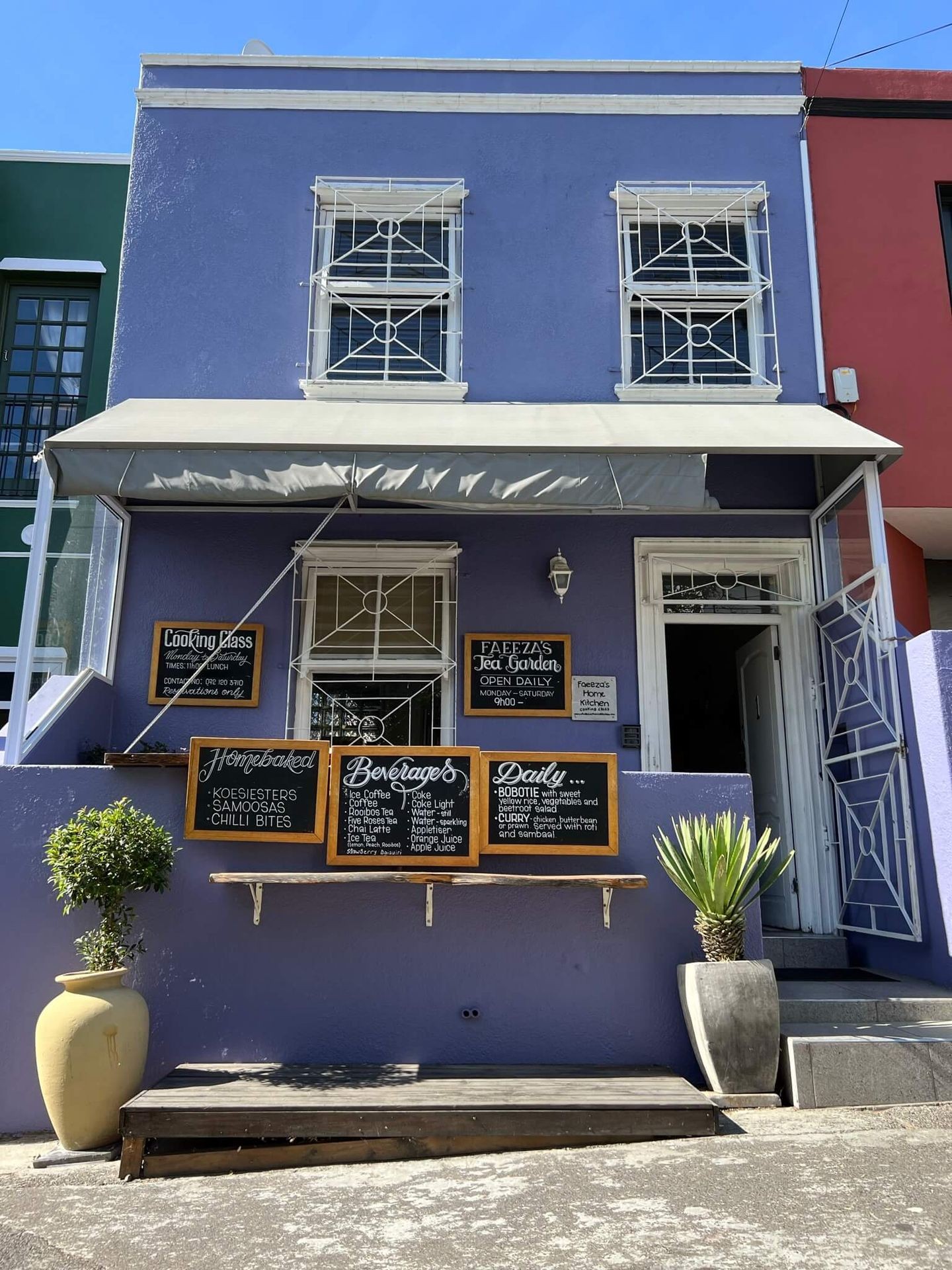 Purple building with menu boards outside for a tea garden, featuring beverages and homebaked goods.