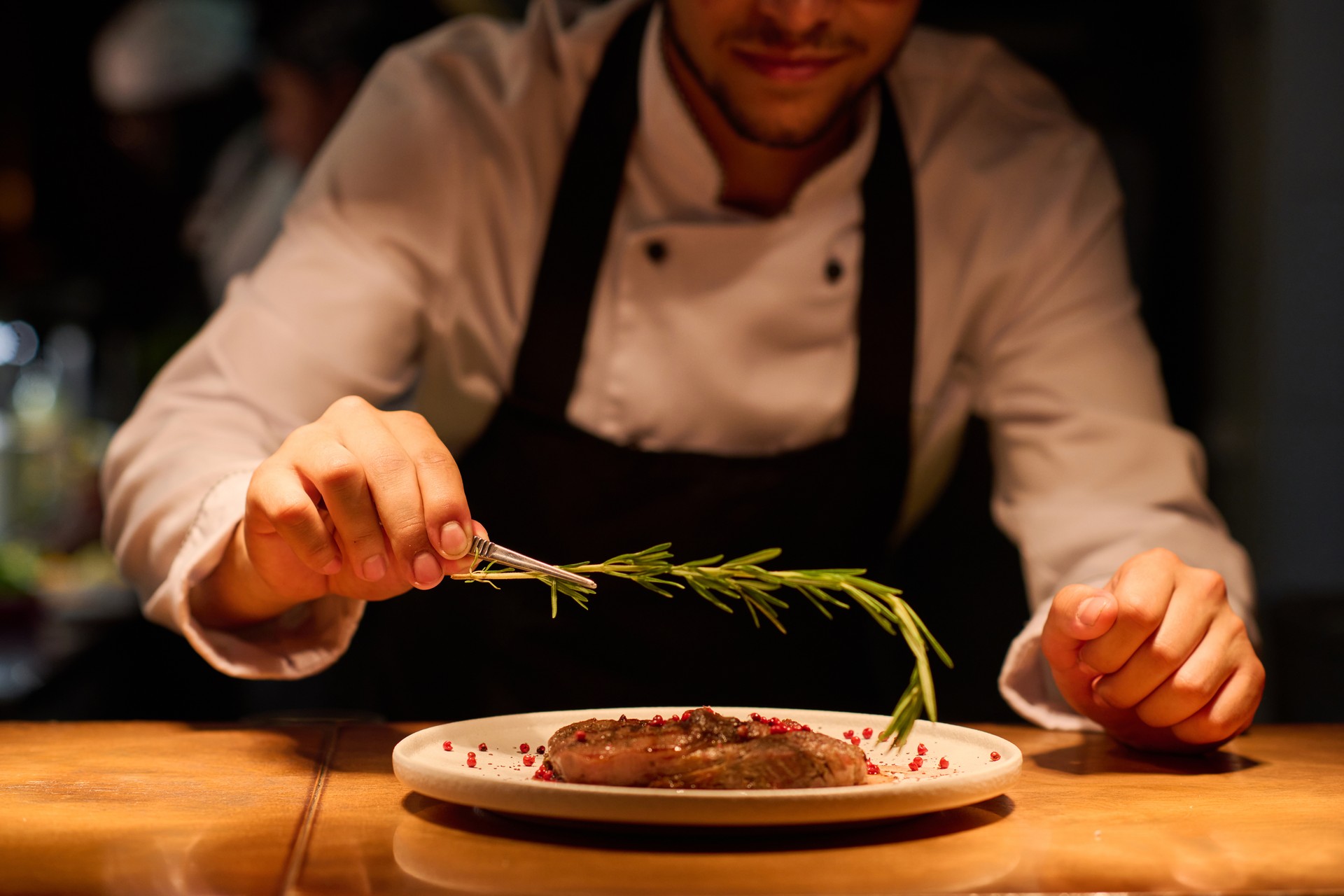 Hand of young male chef putting aromatic herb on top of roasted meat